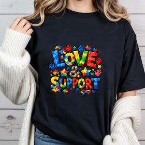May include: A navy blue t-shirt with the words "LOVE & SUPPORT" in colorful puzzle piece letters. The design includes stars, paw prints, and an infinity symbol, all in vibrant colors.