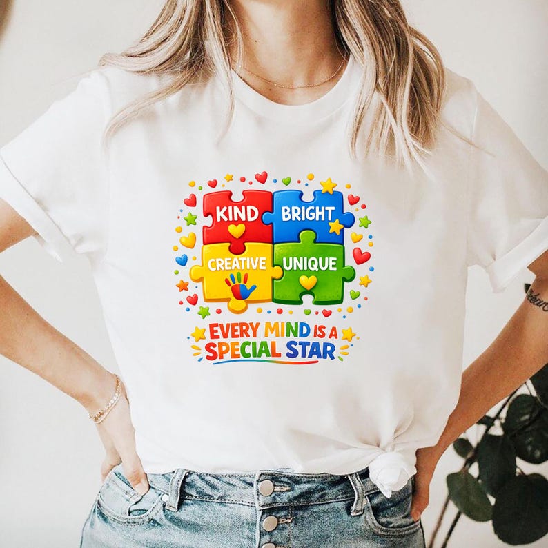 May include: White t-shirt featuring a colorful puzzle design with the words "KIND, BRIGHT, CREATIVE, UNIQUE" and "EVERY MIND IS A SPECIAL STAR". The design includes hearts, stars, and handprints.