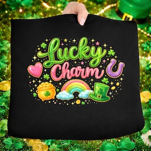 Puede incluir: Cojín negro con un diseño colorido de "Lucky Charm". El diseño incluye un arcoíris, una olla de oro, una herradura, un corazón y un sombrero verde de duende. Las palabras "Lucky Charm" están en verde y rosa.
