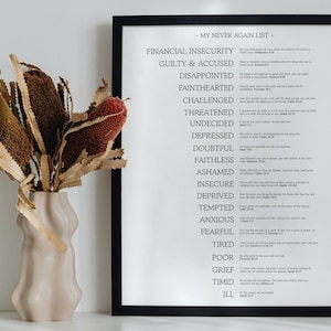 Puede incluir: Una impresión en blanco y negro enmarcada titulada "MY NEVER AGAIN LIST" con una lista de emociones negativas. Un jarrón beige con flores secas está a la izquierda. El jarrón tiene un diseño ondulado único. Las flores son marrones, verdes y rojas.