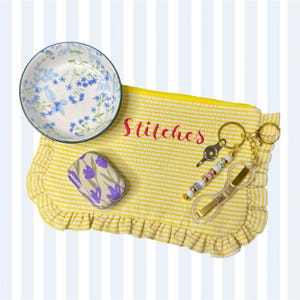 May include: A yellow and white striped ruffled pouch with the word Stitches embroidered in red, a small floral bowl, a rectangular tin with purple tulips, and a gold-toned keychain with beads and a clear plastic thread cutter tool.