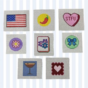May include: A collection of needlepoint canvases featuring various designs. Includes an American flag, a red chili pepper on a yellow circle, a pink heart with "STFU" text, a purple flower, a floral design, a blue bow, a cocktail glass, and a heart.