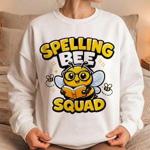May include: A white crewneck sweatshirt featuring a graphic of a yellow bee wearing black glasses and reading an open book. The text "SPELLING BEE SQUAD" is printed in bold yellow letters with black outlines above and below the bee illustration.