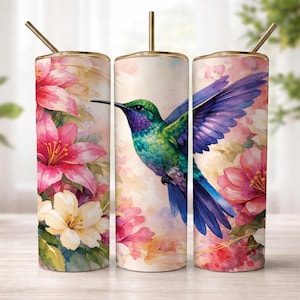 May include: Three stainless steel tumblers with gold lids and straws. Each has a watercolour design of a hummingbird with purple and green feathers, surrounded by pink and white flowers. The background has a soft, pastel colour palette.