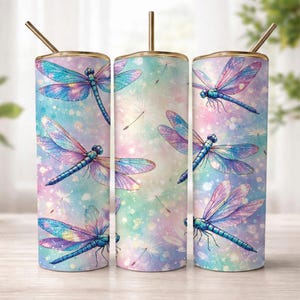 May include: Three stainless steel tumblers with a dragonfly design. The tumblers feature a pastel watercolor background with blue, purple, and pink dragonflies. Each tumbler has a gold-colored rim and straw.