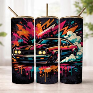 May include: A cylindrical tumbler with a straw featuring a vibrant graffiti-style print of a classic muscle car. The design includes bright orange, pink, and blue paint splatters against a dark brick wall background with stylised smoke and lightning.