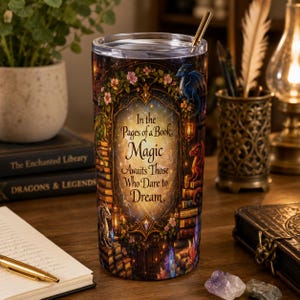 May include: A cylindrical tumbler with a clear lid and a gold metal straw. The exterior features a colourful illustration of a library archway, dragons, and flowers, with the text: In the Pages of a Book, Magic Awaits Those Who Dare to Dream.