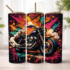 May include: A cylindrical tumbler with a straw featuring a vibrant graffiti-style print of a motorcycle against a brick wall background. The design incorporates splashes of bright orange, pink, and teal paint, with white smoke billowing from the exhaust.