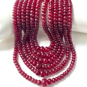 Peut inclure: Une collection de perles en pierre précieuse rouge foncé, rondes et polies, enfilées sur plusieurs brins verticaux. Les perles varient légèrement en taille et en forme, présentant une surface lisse et réfléchissante avec des nuances naturelles.