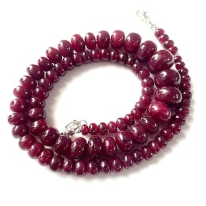 Peut inclure: Un collier composé de perles de pierres précieuses rondes, polies et d'un rouge profond, de tailles variées, disposées en dégradé. Les perles sont enfilées ensemble et fixées par un fermoir en métal argenté aux extrémités, formant un cercle.