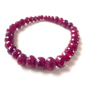 Può includere: Un braccialetto elastico circolare composto da numerose piccole perle di pietre preziose sfaccettate di colore magenta intenso. Le perle sono disposte in un cerchio continuo, mostrando una superficie riflettente e sfaccettata.
