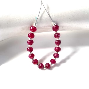 Peut inclure: Un brin de perles de rubis facettées rouge foncé disposées en forme de U. Les petites pierres précieuses rondes et translucides sont séparées par de minuscules perles d'espacement en métal argenté, le tout enfilé sur un fil fin et flexible.
