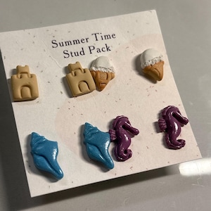 May include: A card featuring six stud earrings with a summer theme. The studs depict sandcastles, ice cream cones, seashells, and seahorses. The card is printed with the text "Summer Time Stud Pack".
