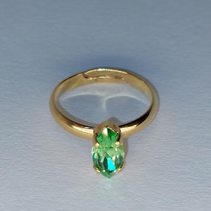 May include: A gold ring with an adjustable band, featuring a marquise-cut, light green gemstone. The gemstone is set in a prong setting. The ring is shown against a light background.