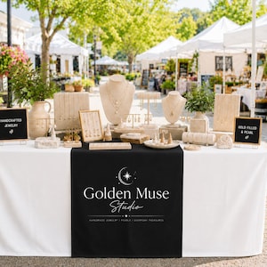 May include: A jewellery display table featuring multiple beige necklace busts, earring stands, and ring cones. Two black signs read "HANDCRAFTED JEWELRY" and "GOLD FILLED & PEARL". A black table runner displays the white text "Golden Muse Studio".