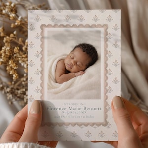 May include: A birth announcement card featuring a sleeping baby wrapped in a blanket. The card has a scalloped border and floral pattern. Text reads "Introducing Florence Marie Bennett, August 4, 202x, 12:48 PM, 9 lbs 6 oz, 21 inches."