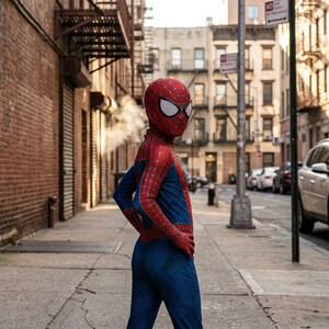 May include: A full-body Spider-Man costume featuring a vibrant red and blue color scheme with a detailed black web pattern across the red sections. The suit includes a matching full-head mask with large white eye lenses and a textured fabric finish.