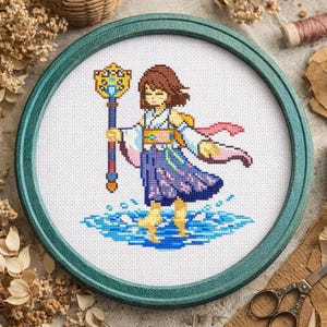 May include: Cross-stitch art of a character from a video game, set in a green circular frame. The character is a woman in a kimono, holding a staff. The background is white, with blue water at the character's feet.