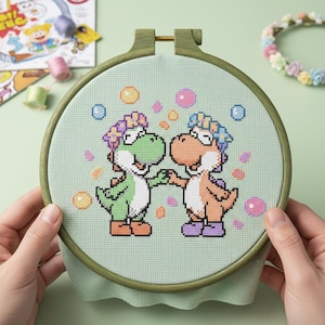 Può includere: Un telaio da ricamo a punto croce con due dinosauri dei cartoni animati che si tengono per mano. I dinosauri sono verdi e arancioni con fasce floreali, circondati da bolle colorate su uno sfondo verde chiaro. Il telaio di legno è tenuto da mani.