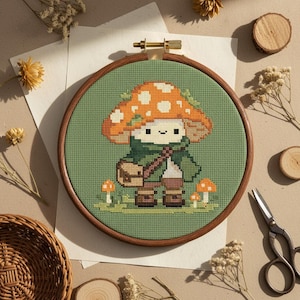 May include: A cross-stitch embroidery hoop featuring a mushroom character with an orange and white spotted cap, green jacket, and brown satchel. The background is a light green fabric, and the wooden hoop is 6 inches in diameter. Two small mushrooms are at the bottom.