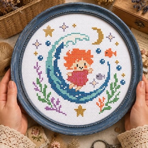 May include: A circular cross-stitch embroidery in a blue frame featuring a character with orange hair and a pink dress riding a large blue wave. The design includes yellow stars, a crescent moon, small fish, and green and purple seaweed elements.
