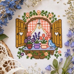 May include: A cross-stitch embroidery on white fabric depicting an open window with wooden shutters, pink gingham curtains, and a window box filled with purple and orange flowers. A small blue bird sits on the ledge among the potted plants.