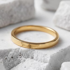 May include: A polished gold band ring with a smooth, flat surface and a circular shape. The ring features a reflective metallic finish and a consistent width throughout the entire circumference of the band, showcasing a simple and clean design.