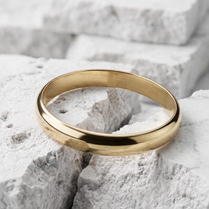 Könnte beinhalten: Ein polierter Goldring mit einer glatten, abgerundeten Außenfläche und einer reflektierenden metallischen Oberfläche. Der Ring hat ein schlichtes, durchgehendes kreisförmiges Design mit gleichbleibender Breite und einem hellen Gelbgoldton.