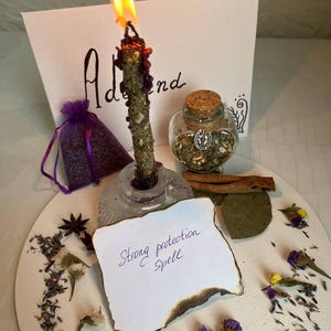 Puede incluir: Una vela encendida con un tallo verde y morado en un soporte de vidrio. Un pequeño frasco de vidrio con tapa de corcho, una bolsa morada y un papel con "Strong protection Spell" también están presentes. Flores y hierbas secas rodean los objetos.