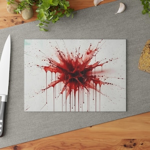 Könnte beinhalten: Rechteckiges Schneidebrett mit einem auffälligen roten Spritzmuster. Das abstrakte Kunstwerk zeigt einen zentralen Ausbruch mit radialen Linien und tropfenden Akzenten, wodurch ein dynamischer visueller Effekt entsteht. Das Brett liegt auf einer Holzoberfläche.