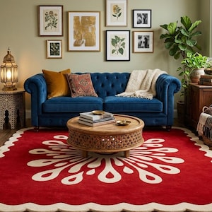 Könnte beinhalten: Ein Wohnzimmer mit einem blauen Samtsofa, Kissen und einem runden Couchtisch aus Holz. Ein roter Teppich mit weißem Blumenmuster liegt auf dem Boden. Botanische Drucke und gerahmte Fotos schmücken die olivgrüne Wand. Eine dekorative Lampe steht auf einem Beistelltisch.