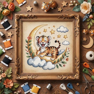 May include: A framed cross-stitch featuring a smiling tiger cub on a crescent moon, surrounded by stars and clouds. The frame is gold-colored, and the scene is set against a neutral background. Decorative elements include spools of thread, wooden stars, and floral accents.