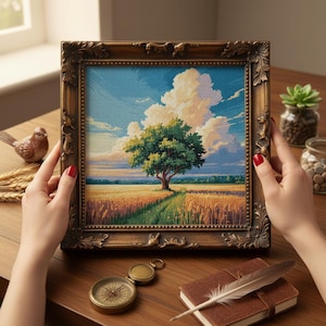 May include: A framed cross-stitch landscape featuring a tree in a field under a blue sky with puffy white clouds. The frame is ornate, with a dark brown finish. The artwork is held by a person with red nail polish.