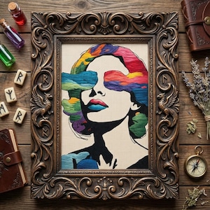 May include: A framed embroidery art piece featuring a woman's face with colorful, abstract cloud-like shapes covering her eyes and hair. The frame is ornate, bronze-colored, and the artwork is set against a neutral background. The piece is surrounded by other items.