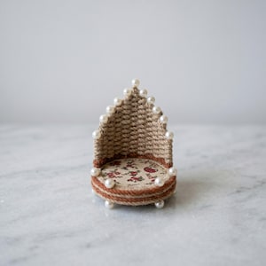 May include: Miniature woven chair with a floral patterned seat and a woven back. The chair is trimmed with a brown border and adorned with faux pearls. The chair is approximately 3 inches tall.