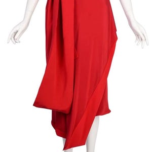May include: A bright red skirt with a wrap-around design. The skirt has a long, flowing sash that wraps around the waist and hangs down the front. The fabric looks lightweight and has a slight sheen.