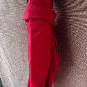 May include: A bright red scarf, neatly folded and draped. The fabric has a subtle texture, and the scarf is neatly arranged, showcasing its rich colour and potential for stylish wear. The scarf is a solid colour.