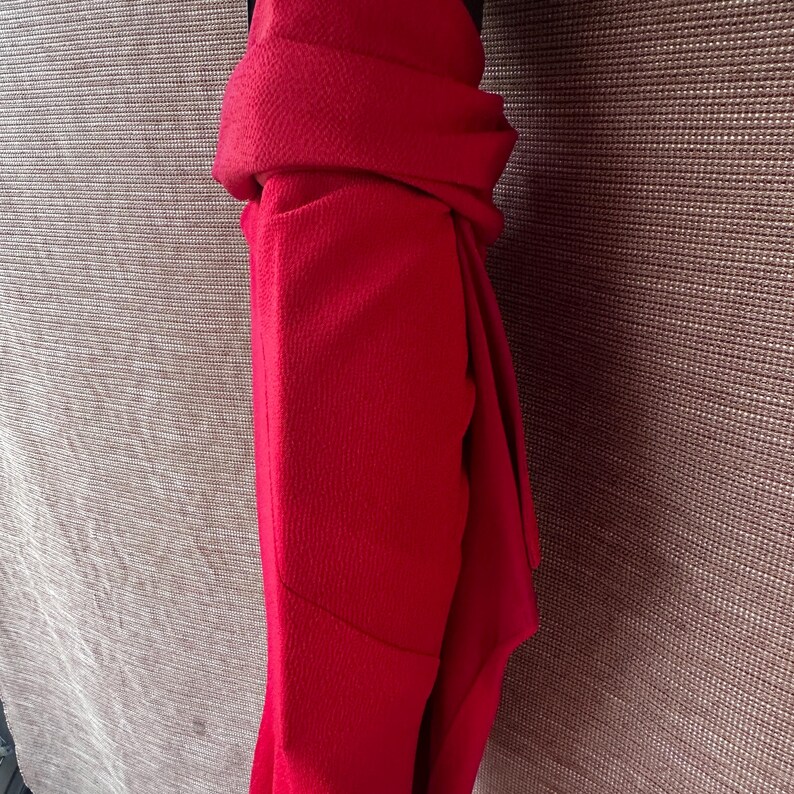 May include: A bright red scarf, neatly folded and draped. The fabric has a subtle texture, and the scarf is neatly arranged, showcasing its rich colour and potential for stylish wear. The scarf is a solid colour.