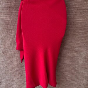 May include: A striking red skirt with a distinctive design. The skirt has a high waist and a draped, flowing fabric, creating an elegant silhouette. The fabric is a smooth, solid colour, suitable for a formal event or special occasion.