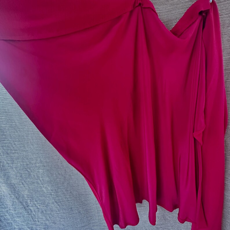 May include: A flowing, magenta-coloured garment, possibly a wrap or skirt, with soft draping and a smooth texture. The fabric is a vibrant, solid colour, and the design suggests a versatile piece of clothing.