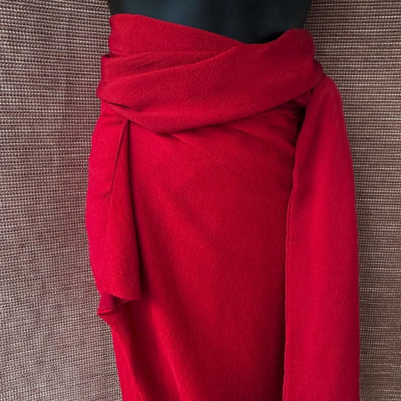 May include: A bright red wrap skirt, displayed on a mannequin. The fabric has a textured appearance, with a flowing design. The skirt is a striking piece, ideal for making a statement. The skirt's design is elegant.