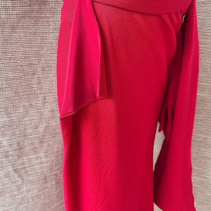 May include: A striking red skirt with a textured fabric and a distinctive wrap design. The skirt has a wide waistband and a flowing, asymmetrical drape, creating a stylish silhouette. The skirt's length is approximately 76 cm.