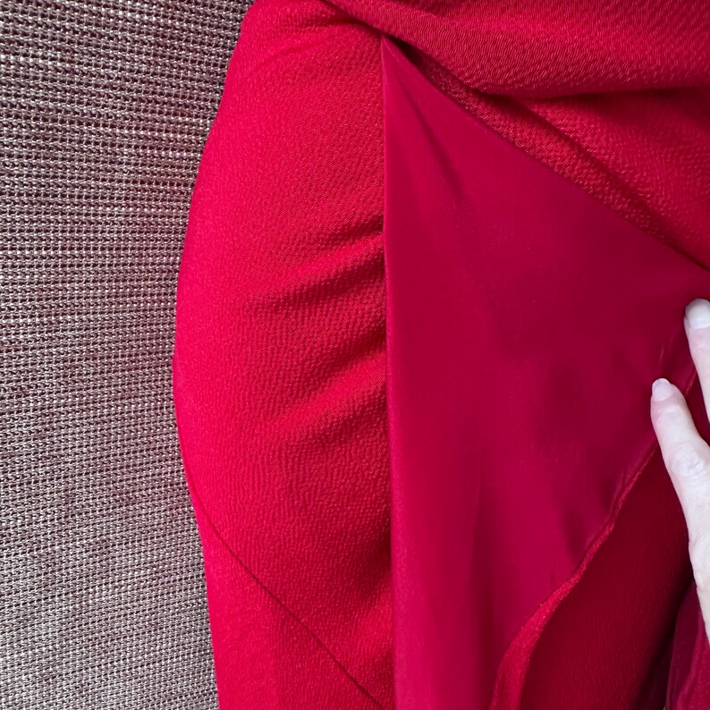 May include: A close-up view of a bright red garment. The outer layer has a textured finish, while the inner lining is smooth. The fabric is draped, highlighting the contrast between the textures and the intense colour.