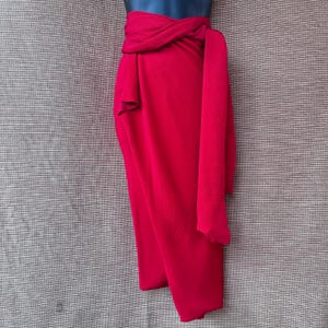 May include: A bright red wrap skirt, tied at the waist with a long sash. The skirt is draped, creating a flowing shape. The fabric is a solid colour, giving a sleek and elegant appearance. The skirt is approximately 90 cm in length.