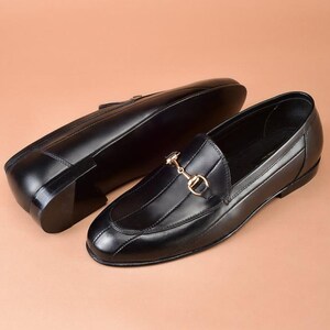 Mocassins masculinos de couro preto, feitos à mão, com bico dividido e detalhe de bridão.