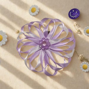 May include: A light purple and silver ribbon flower hair clip with a central jewel embellishment. The clip is surrounded by daisy and smiley face decorative pins.