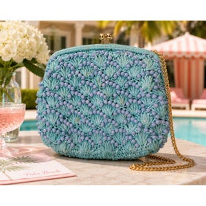 May include: A light blue woven clutch bag featuring a textured fan-shaped pattern accented with small matching beads. The bag has a gold-toned metal frame closure at the top and a long, thin gold-toned metal chain strap attached to the sides.