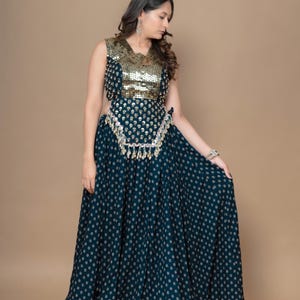 May include: A sleeveless dark teal floor-length dress featuring a gold sequined bodice and a waist panel adorned with hanging metallic coins. The skirt is decorated with a repeating small gold floral pattern, creating a cohesive look.