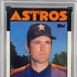 May include: A 1986 Topps Nolan Ryan baseball card, graded PSA 8 NM-MT, featuring a portrait of the player in an Astros cap and jersey. The card displays the text ASTROS, Topps, P, Astros, and NOLAN RYAN, encased in a clear protective plastic slab.