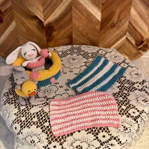 May include: A set of handmade crochet items including a white rabbit and a gray rabbit sitting in a yellow and teal pool float with pink polka dots, a small yellow duck, a teal and white striped rectangular piece, and a pink and white striped piece.